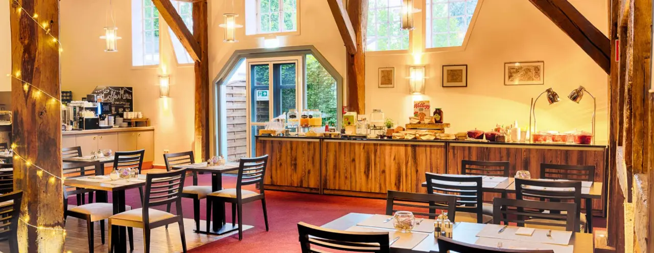 Einladender Frühstücksbereich mit reichhaltigem Buffet und rustikalen Holzbalken im Welcome Hotel Bad Arolsen.