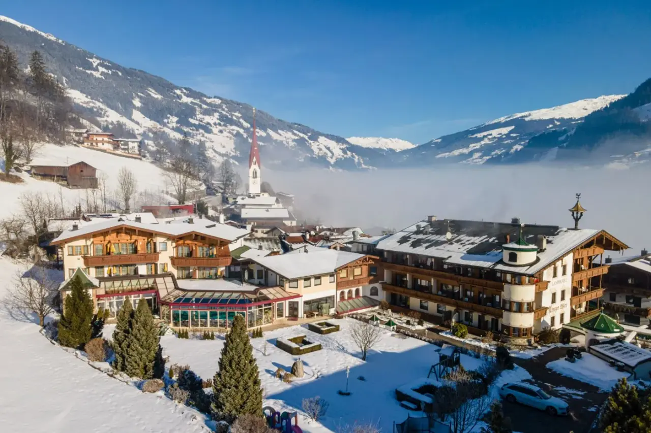 Winterliche Aussenansicht des Landhotel Zenzerwirt mit Poolbereich, umgeben von verschneiten Bergen und Dorf.