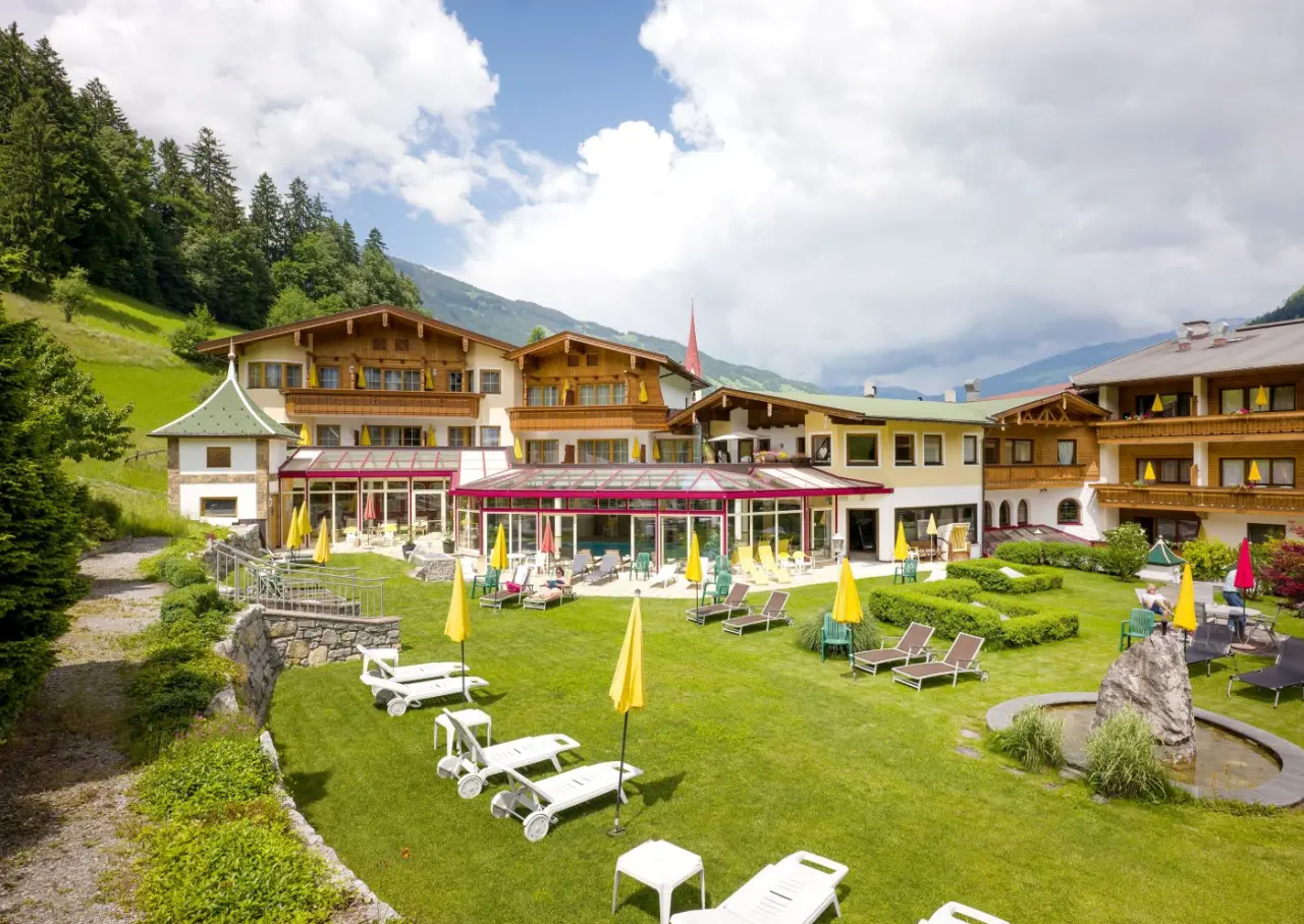 Landhotel Zenzerwirt mit traditioneller Architektur, gepflegtem Garten, Liegewiesen und Alpenpanorama unter blauem Himmel.