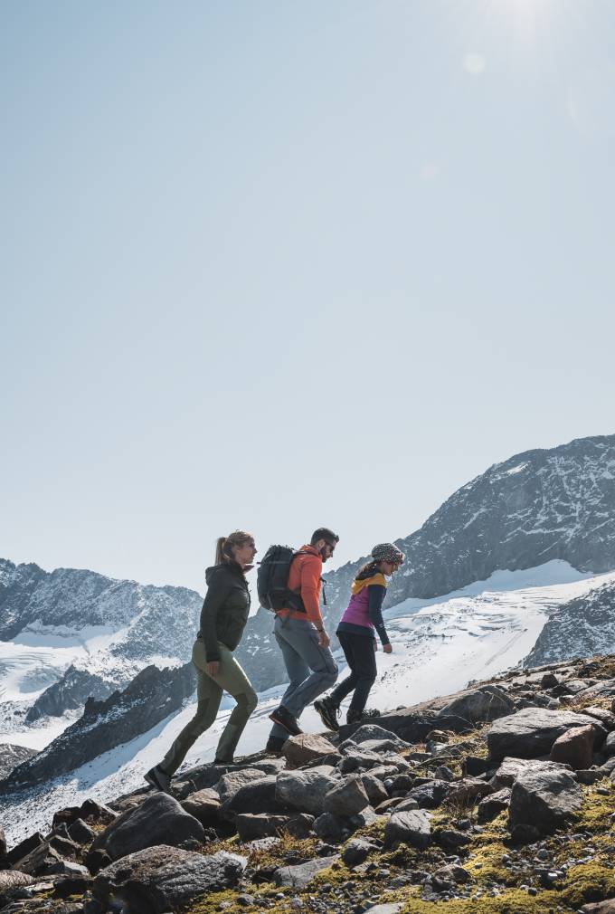 Alpenhotel Kindl in Neustift – Wanderer auf felsigem Bergpfad mit schneebedeckten Gipfeln | Wellnesshotel Stubaital