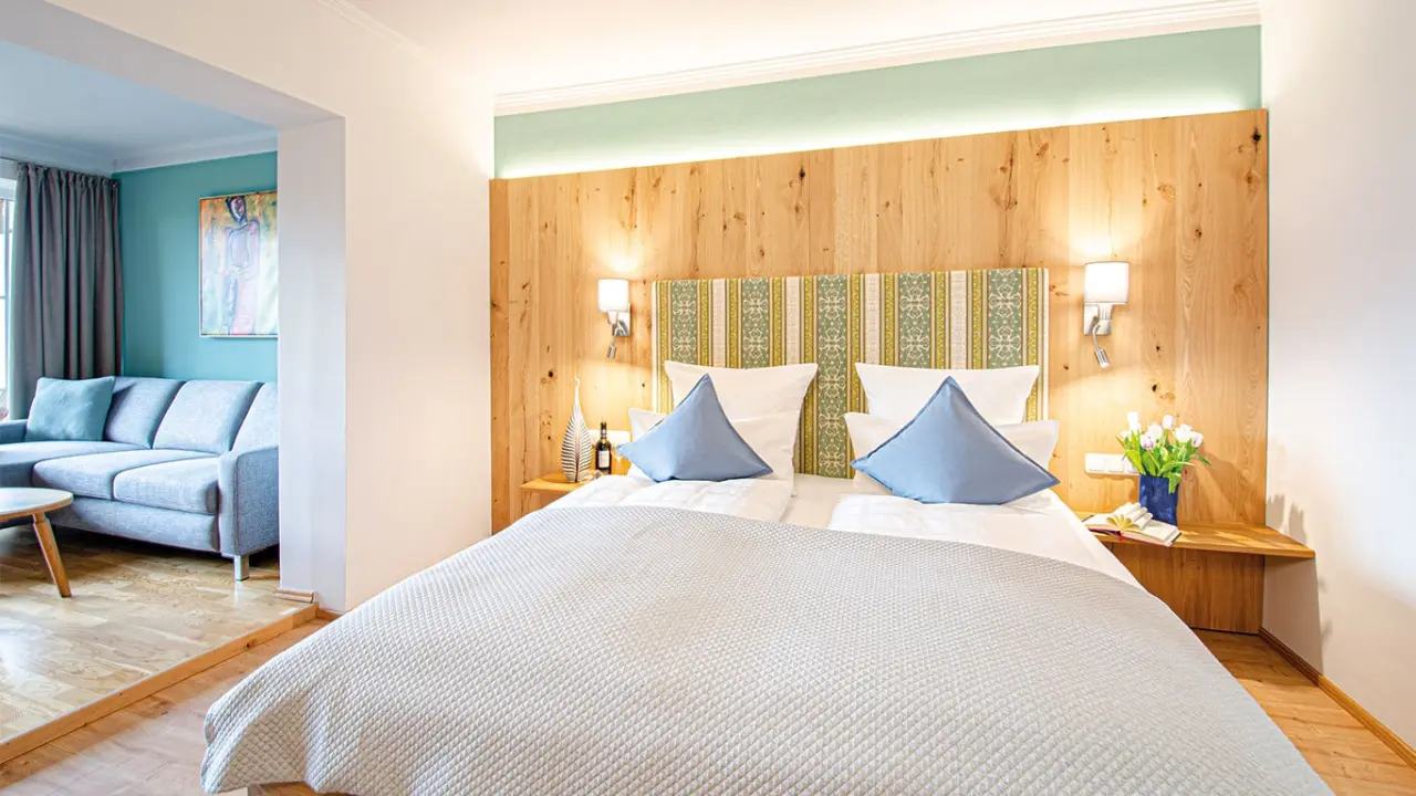 Geräumige Suite im Glashotel Zwiesel mit gemütlichem Doppelbett, Holzkopfteil und separatem Wohnbereich.