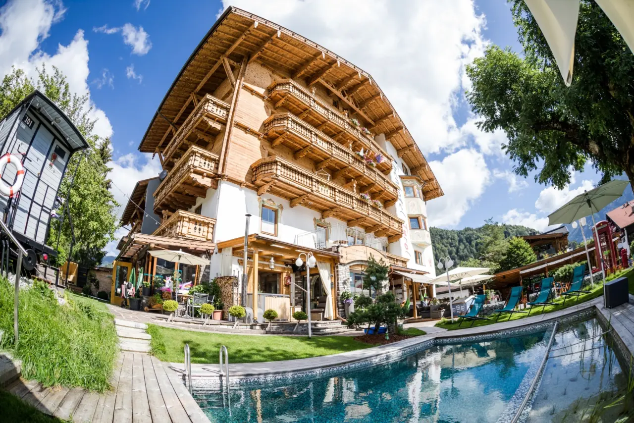 Aussenansicht des Alpenhotel Tyrol am Achensee mit Pool, Liegewiese und traditioneller Holzarchitektur unter blauem Himmel.