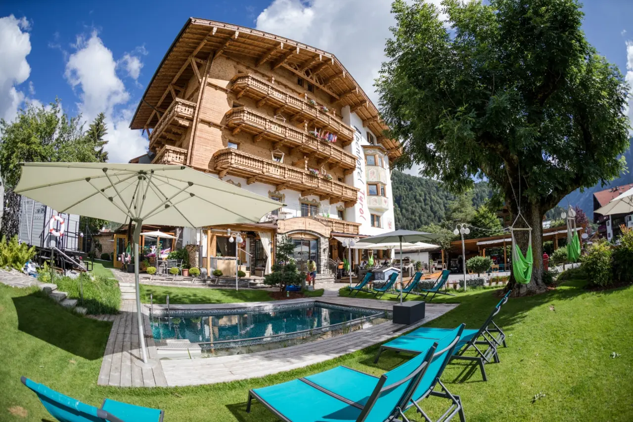 Aussenansicht des Alpenhotel Tyrol mit Pool, Liegewiese und Bergblick am Achensee an einem sonnigen Tag.