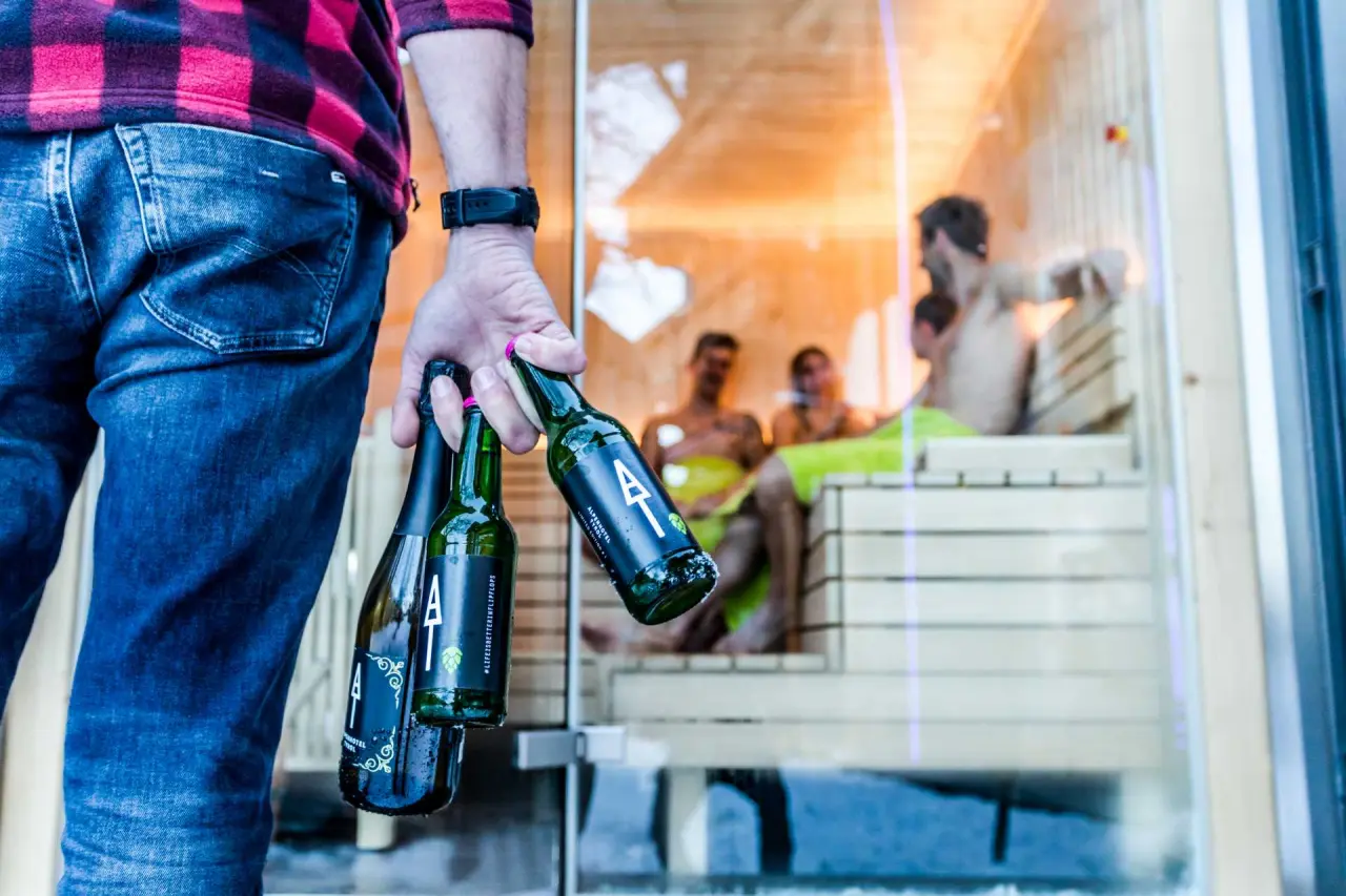 Gast mit Alpenhotel Tyrol Bierflaschen vor einer entspannten Sauna im 4* Adults Only Hotel am Achensee.