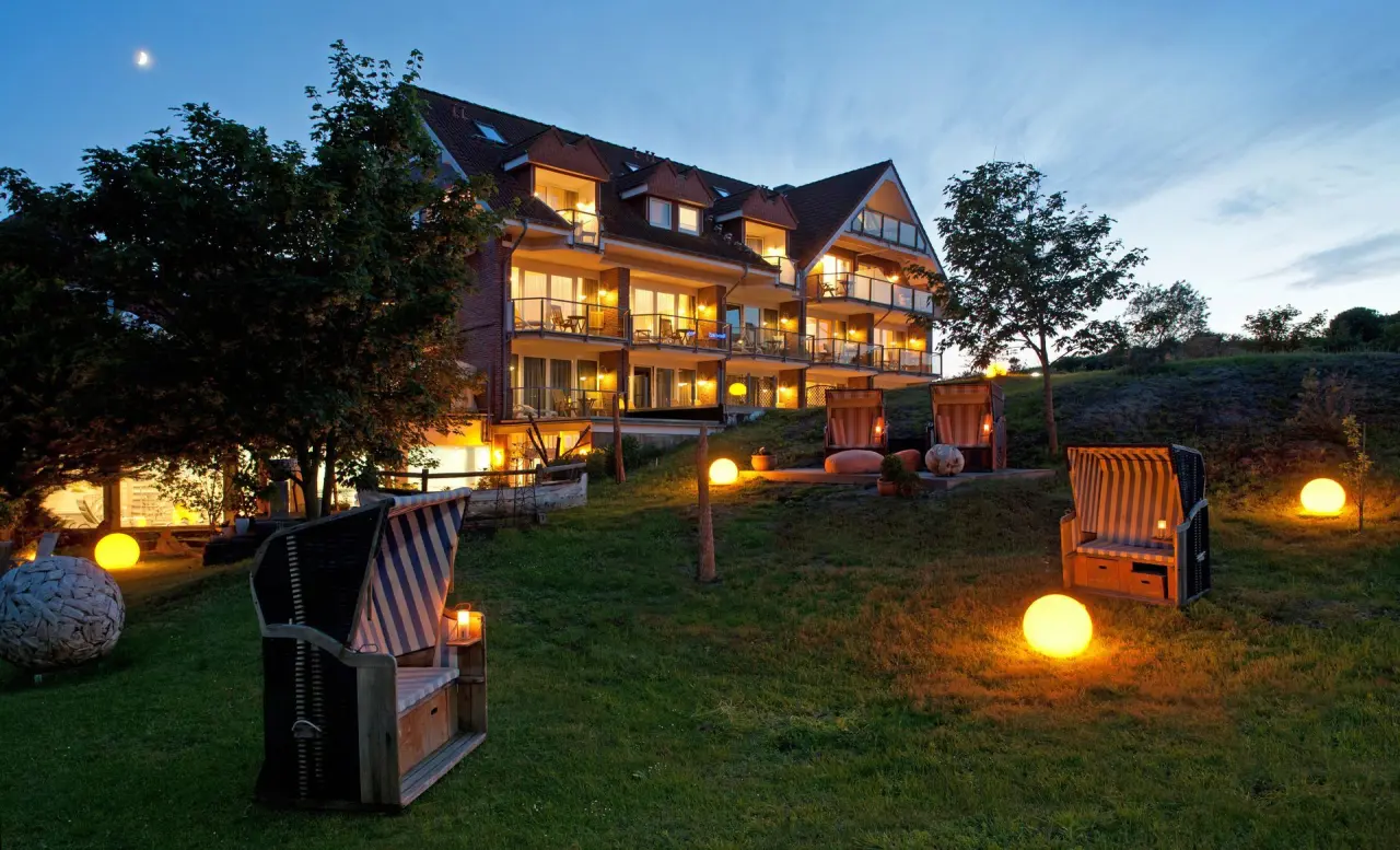 Beleuchtetes Hotel Pabst bei Abenddämmerung mit gemütlichem Garten und Strandkörben. Einladende Aussenansicht.