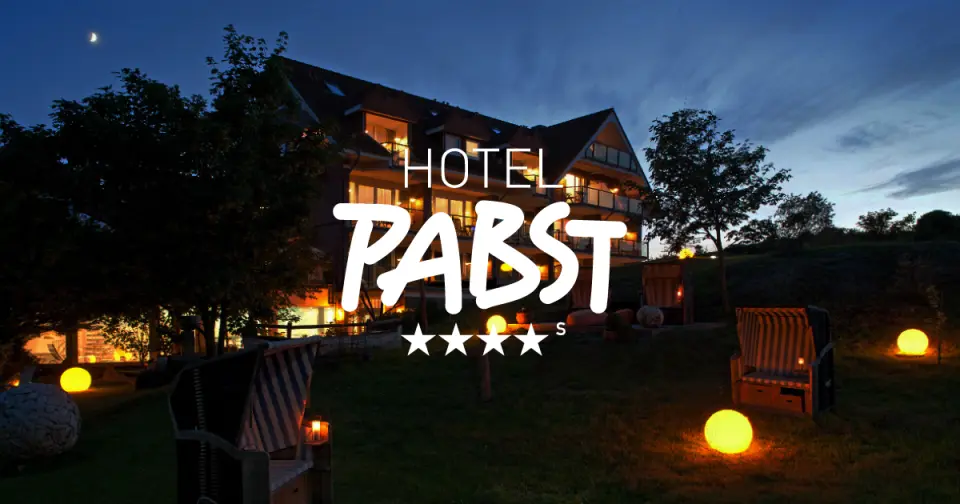 Abendliche Aussenansicht des Hotel Pabst mit beleuchteter Fassade, Strandkörben und leuchtenden Kugeln im Garten unter dem Mond.