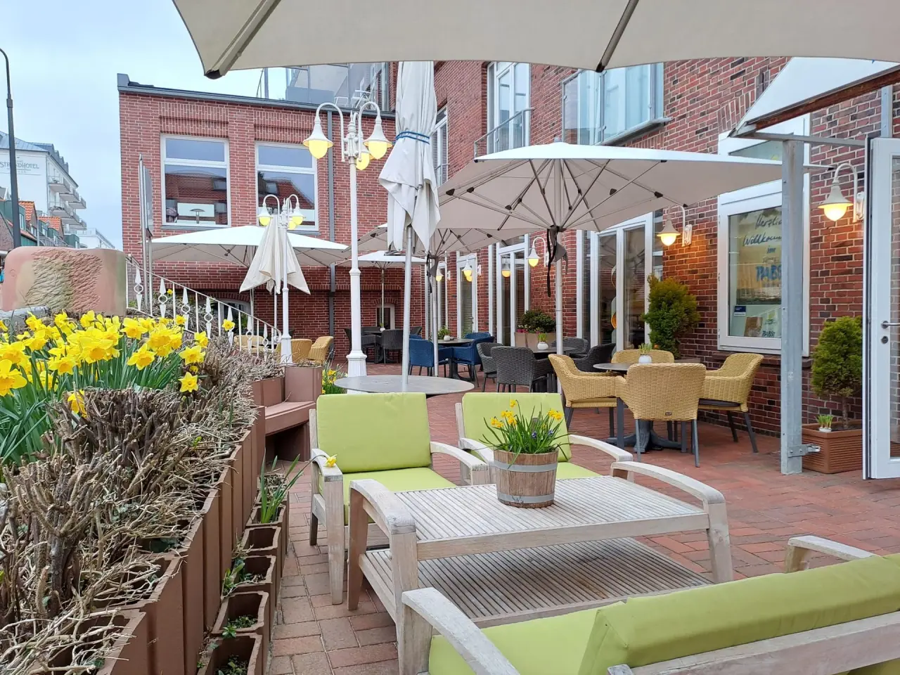 Einladende Gartenterrasse des Hotel Pabst mit bequemen Sitzgelegenheiten, Sonnenschirmen und blühenden Narzissen.