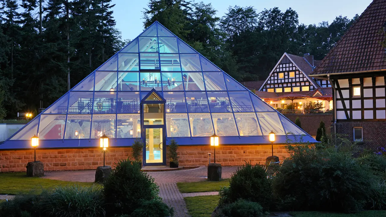 Einladender Poolbereich in der markanten Glaspyramide des Vila Vita Burghotel Dinklage bei Abendbeleuchtung.
