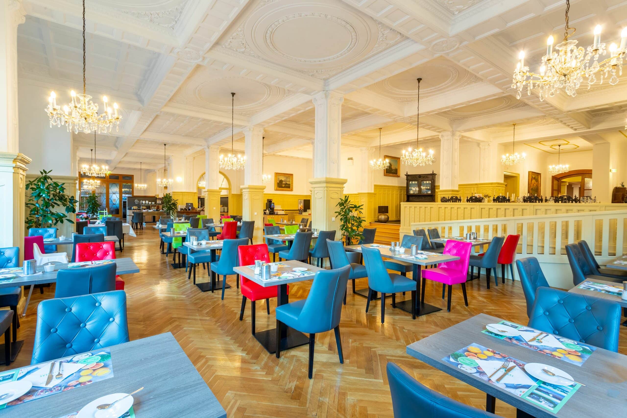 Hotel Badehof in Bad Salzschlirf – Großer Speisesaal mit Kronleuchtern und bunten Stühlen | Wellnesshotel Hessen