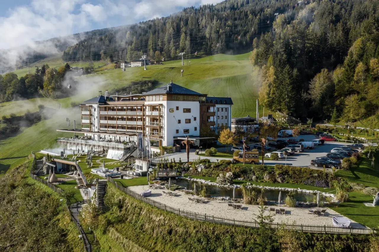 Panoramablick auf das Wellnesshotel DAS.GOLDBERG in den Alpen mit Infinity-Pool, Sonnenterrassen und Bergkulisse.