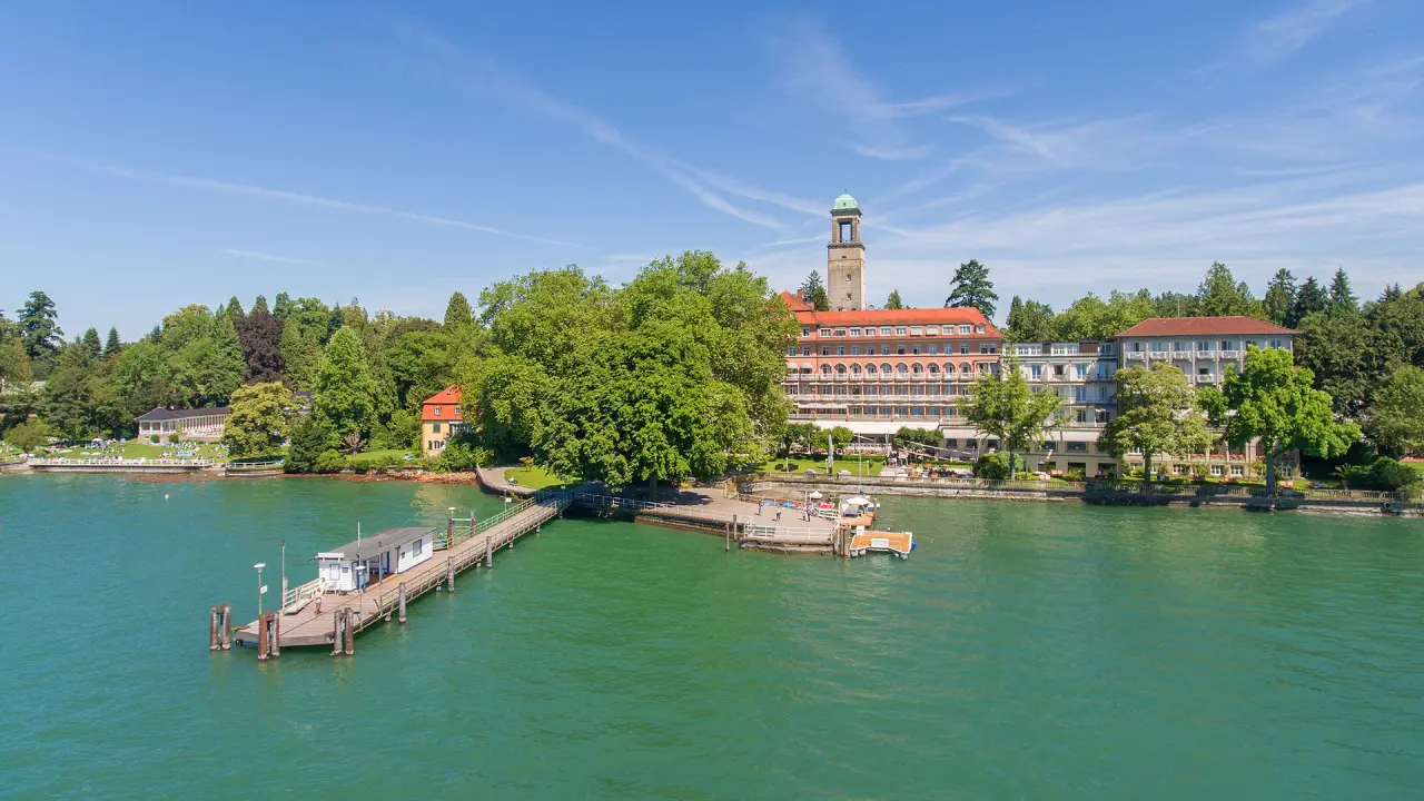 Historisches Hotel Bad Schachen am Bodensee mit eigenem Bootssteg und weitläufiger Parkanlage unter blauem Himmel.