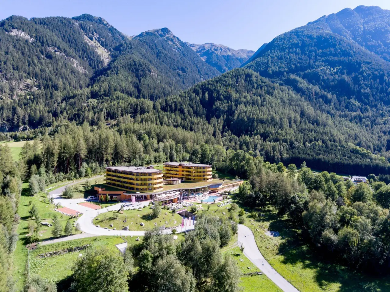 Luftaufnahme des Vivea 4* Hotel Umhausen im Ötztal mit moderner Architektur, Aussenpool und umliegender Berglandschaft.