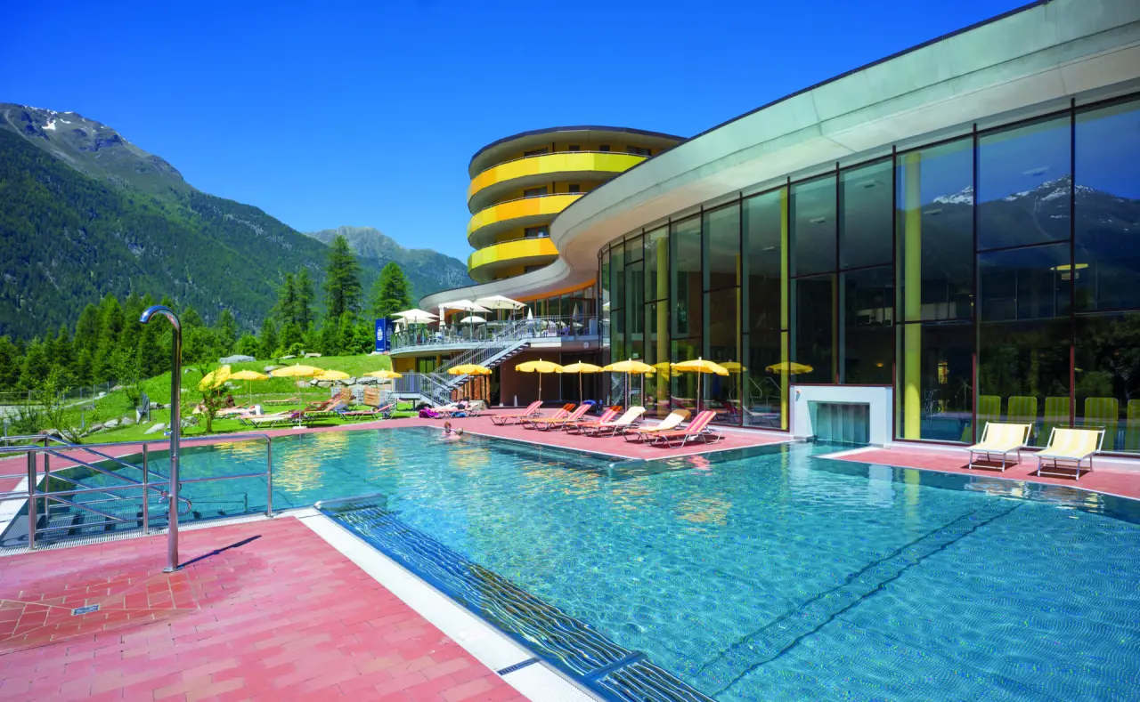 Grosszuegiger Aussenpool mit moderner Hotelarchitektur und Alpenpanorama im Vivea 4* Hotel Umhausen im Ötztal.
