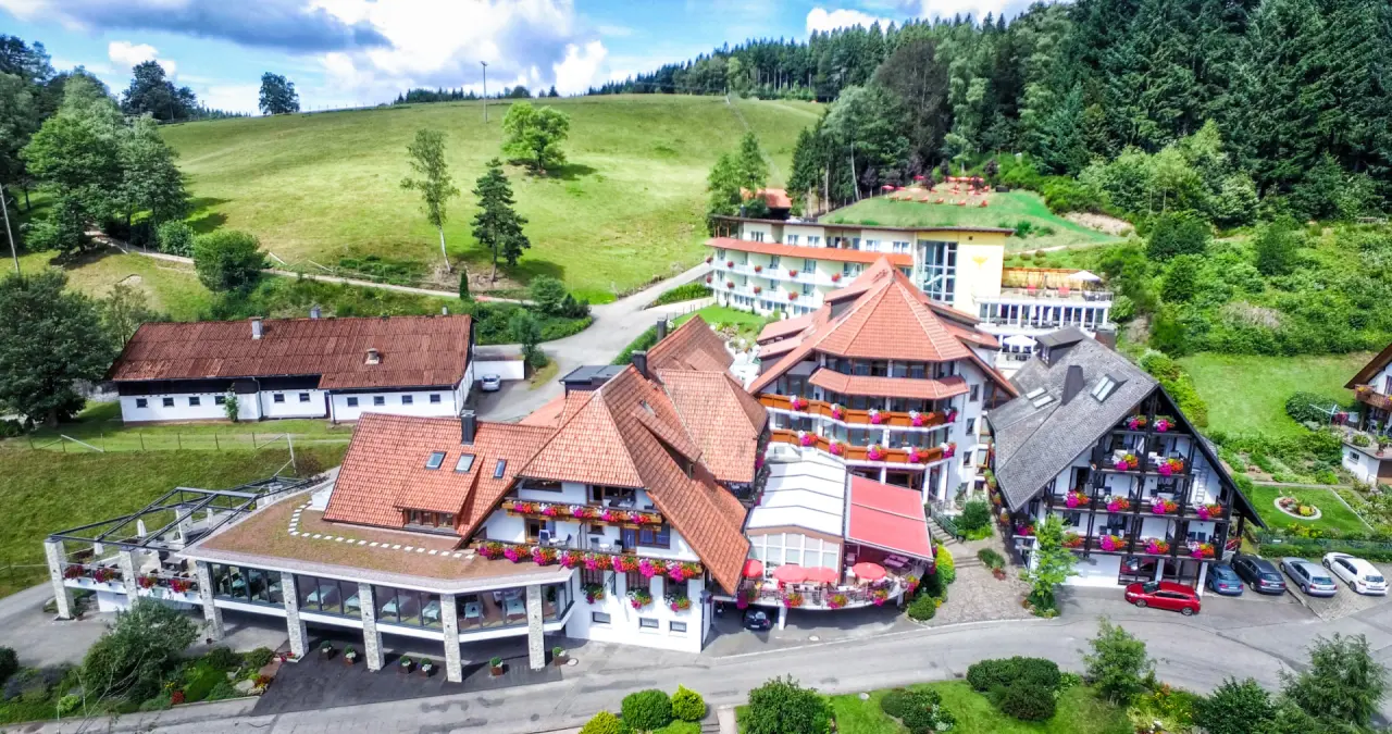 Luftbild des Naturparkhotel Adler St. Roman, eingebettet in grüne Hügel und Wälder des Schwarzwalds, mit blühenden Balkonen.