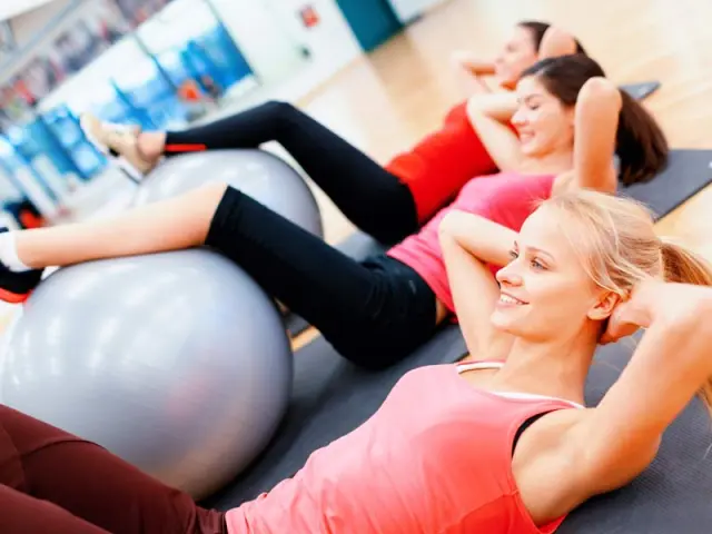 Drei lächelnde Frauen beim Fitnesstraining mit Gymnastikbällen im modernen Fitnessbereich des Naturparkhotel Adler St. Roman.