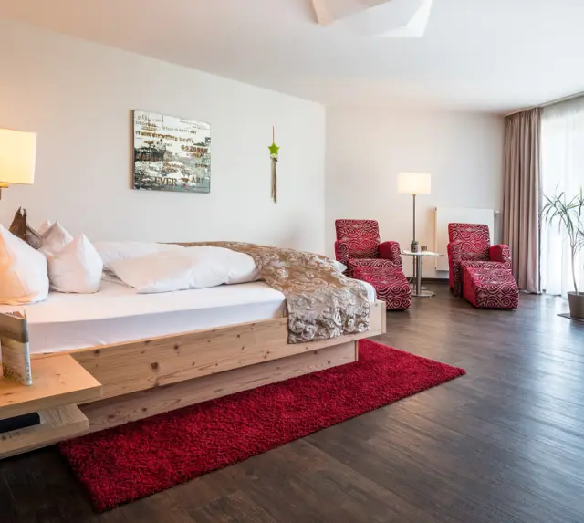 Gemütliches Doppelzimmer mit Holzbett und rotem Teppich im Naturparkhotel Adler St. Roman.