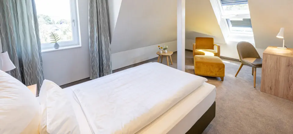 Helles und gemütliches Doppelzimmer im Dachgeschoss des Hotel Noltmann-Peters mit Bett, Sessel und Schreibtisch.