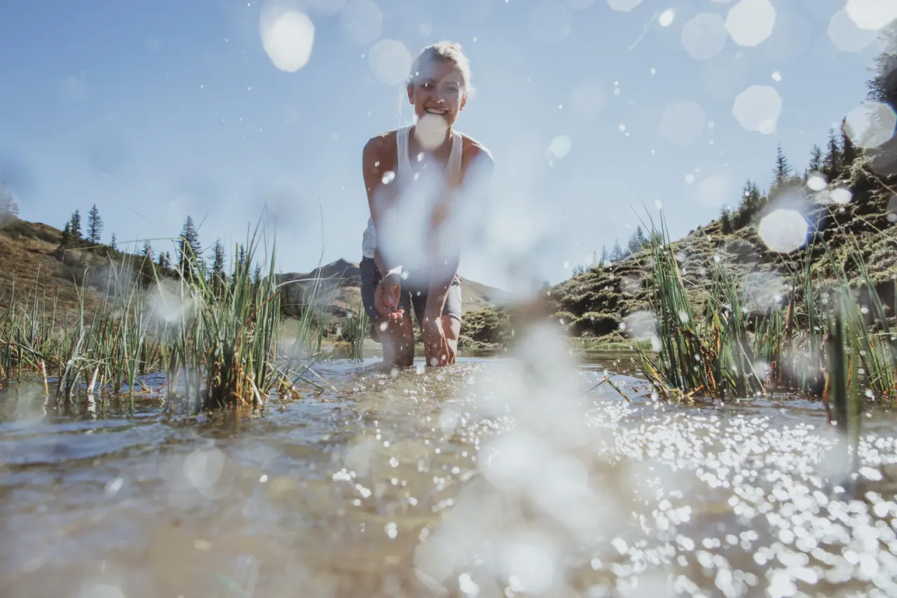 Lachende Frau beim erfrischenden Wassertreten in einem alpinen Bergbach, umgeben von grüner Natur, nahe Hotel Tauernhof.