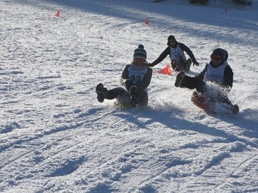Drei Personen rodeln einen verschneiten Hang hinunter im VALAVIER Aktivresort, das Winteraktivitäten anbietet.