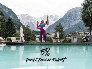 VALAVIER Aktivresort: Paar beim Yoga am Aussenpool mit majestätischem Bergpanorama. Perfekt für Wellness & Sport.