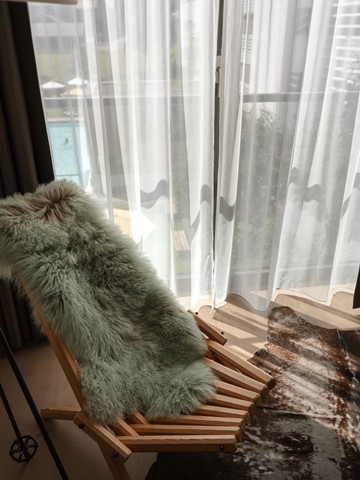 Gemütlicher Sessel mit Schaffell vor Fenster mit Blick auf den Pool im VALAVIER Aktivresort.