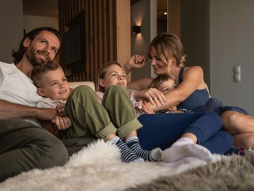 Glückliche Familie entspannt auf dem Sofa in einer gemütlichen Suite des VALAVIER Aktivresorts.