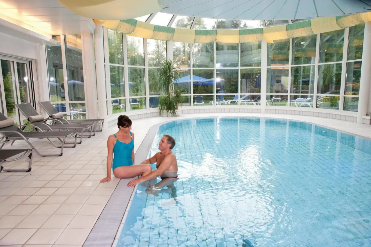 Paar entspannt am Innenpool mit grossen Fenstern und Blick ins Grüne im EurothermenResort Bad Hall - Hotel Miraverde.