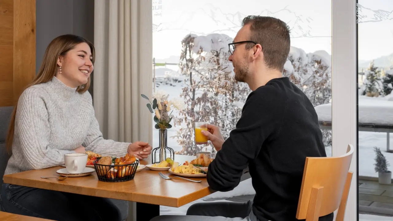 Glückliches Paar beim Frühstück mit verschneitem Bergblick im Restaurant des Hotel Das Weitblick Allgäu.