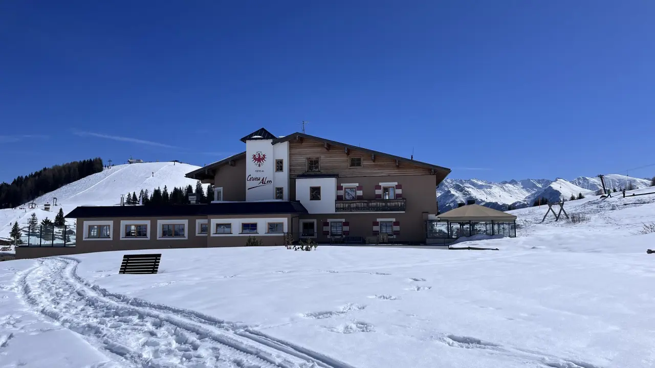 Aussenansicht des Wellness Hotel Cervosa Alm im Winter mit verschneiten Bergen und Skipisten im Hintergrund.