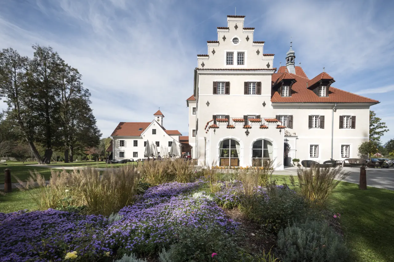 Malerische Aussenansicht des G’Schlössl Murtal mit markantem Giebel, blühendem Garten und strahlend blauem Himmel.