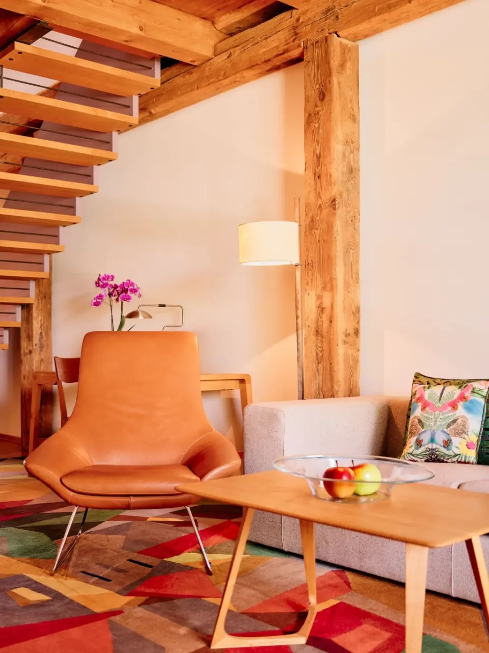 Gemütlicher Wohnbereich einer Suite im G’Schlössl Murtal mit Ledersessel, Sofa, Holzbalken und moderner Treppe.