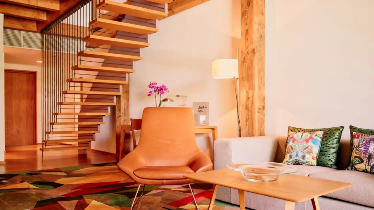 Gemütlicher Wohnbereich mit Holztreppe, Ledersessel und Sofa im G’Schlössl Murtal. Modernes Design für entspannte Stunden.