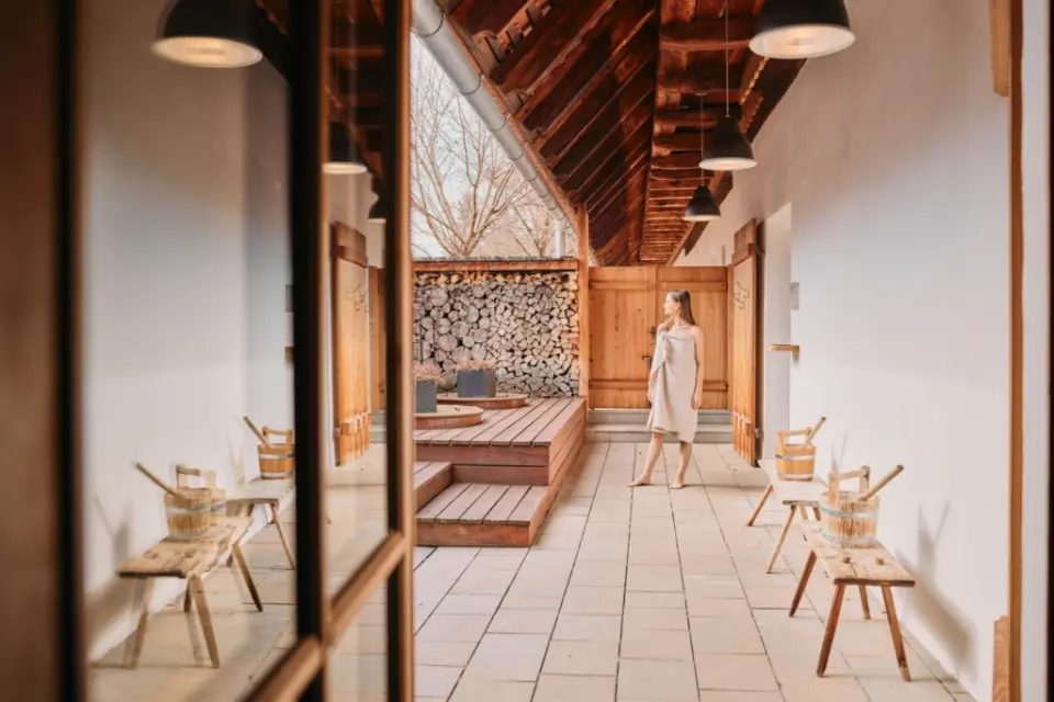Frau im Bademantel im rustikalen Saunabereich mit Holz und Stein im G’Schlössl Murtal. Einladende Wellness-Atmosphäre.