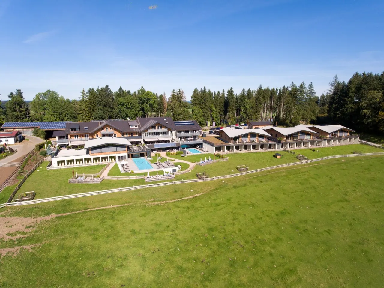 Luftaufnahme des Land- & Wellnesshotel Panorama mit Pools, umgeben von grünen Wiesen und Wald unter blauem Himmel.