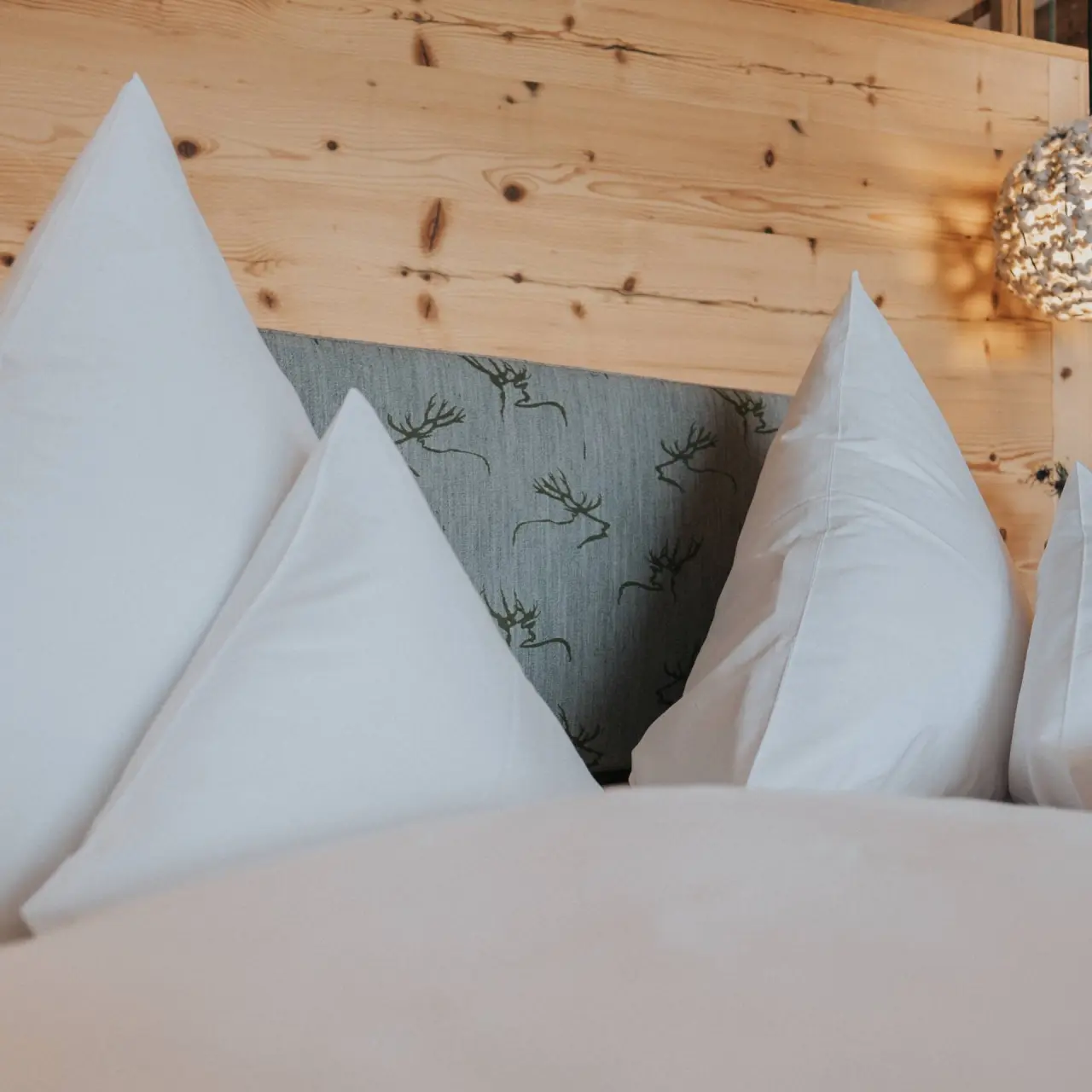 Gemütliches Bett mit weißen Kissen und Hirschgeweih-Muster am Kopfteil im Land- & Wellnesshotel Panorama.