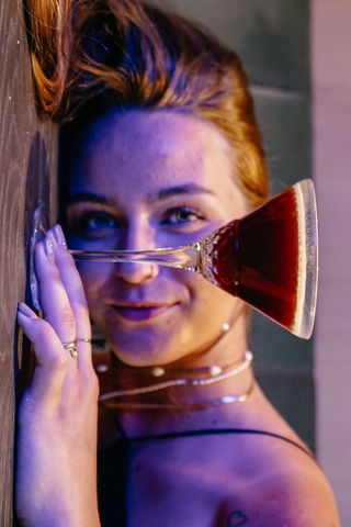 Porträt einer jungen Frau mit rotem Cocktailglas und Perlenkette in stimmungsvoller blauer Beleuchtung im Hotel Alte Post.