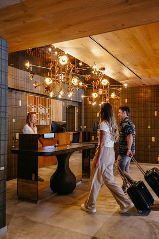 Moderne Hotellobby des Hotel Alte Post mit Rezeption, einzigartiger Deckenlampe und ankommenden Gästen mit Gepäck.