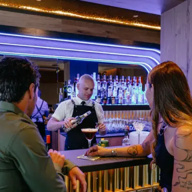Moderne Hotelbar 'Alte Post' mit Barkeeper bei der Zubereitung von Cocktails für Gäste in stilvoller Atmosphäre.