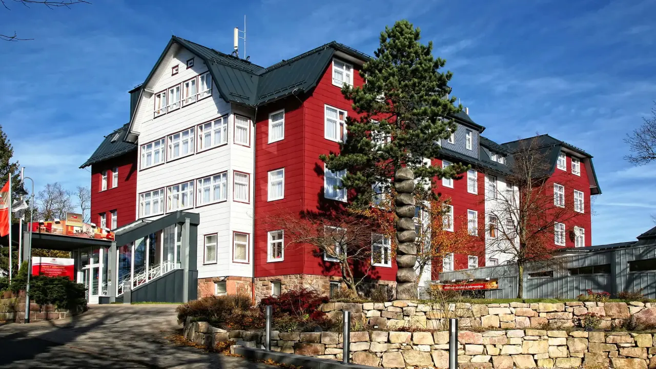 Aussenansicht des Konsum Berghotel Oberhof mit markanter rot-weisser Fassade unter blauem Himmel.