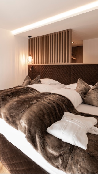 Modernes Doppelzimmer mit Holzelementen, kuscheliger Decke und Bademantel im Hotel Post Ischgl.