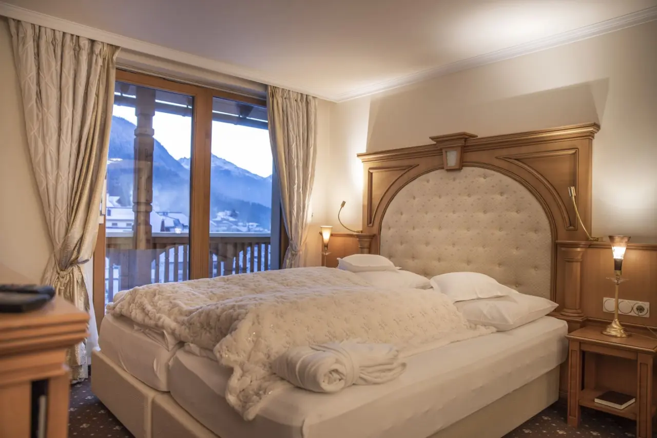 Gemütliches Doppelzimmer im Hotel Post Ischgl mit komfortablem Bett, Holzelementen und Balkonblick auf die Berge.