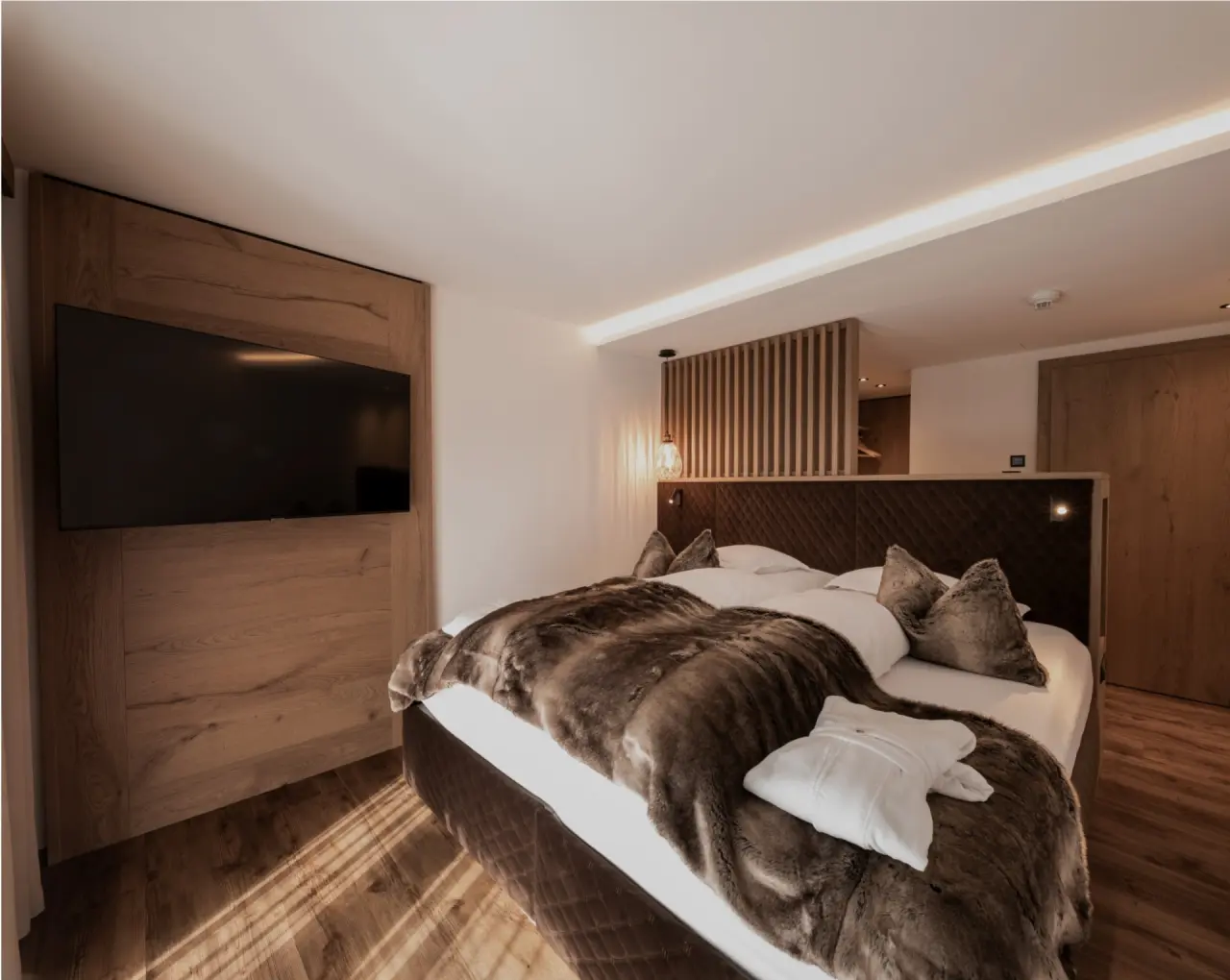 Modernes Doppelzimmer mit Holzelementen, großem Bett, flauschiger Decke und TV im Hotel Post Ischgl.