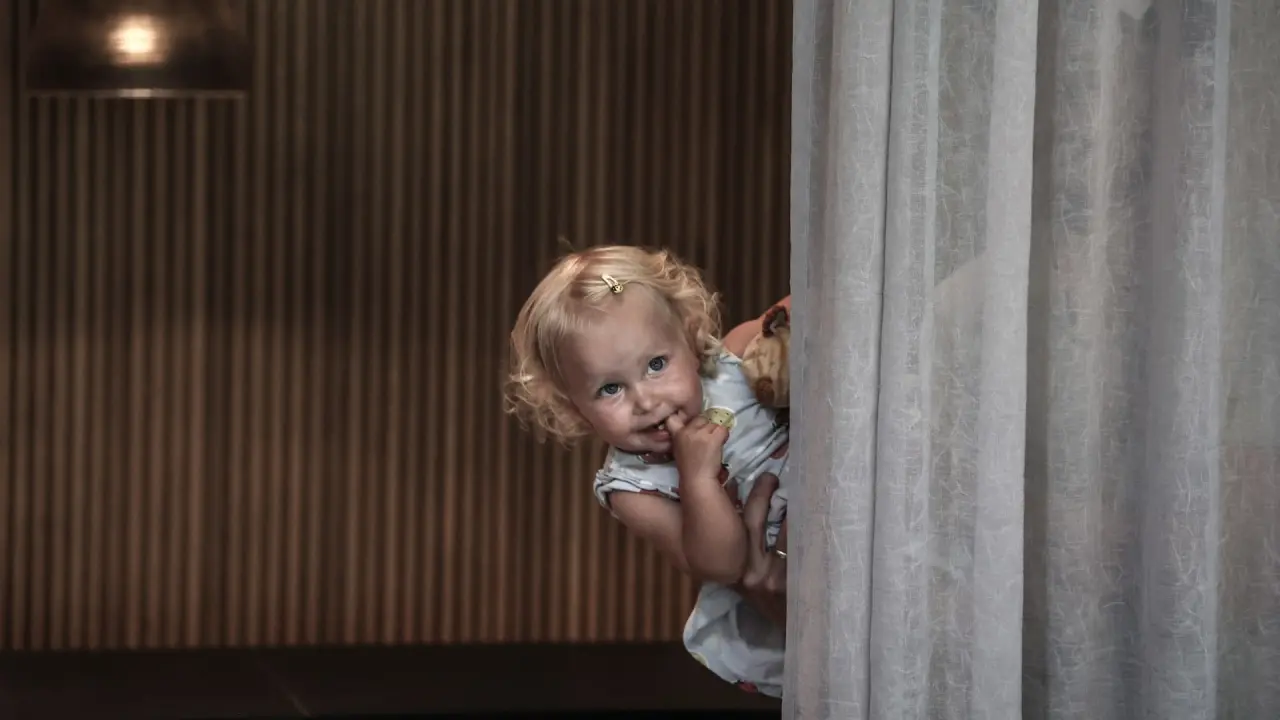 Kleines Kind schaut neugierig hinter einem Vorhang hervor im Almhof Family Resort & SPA.