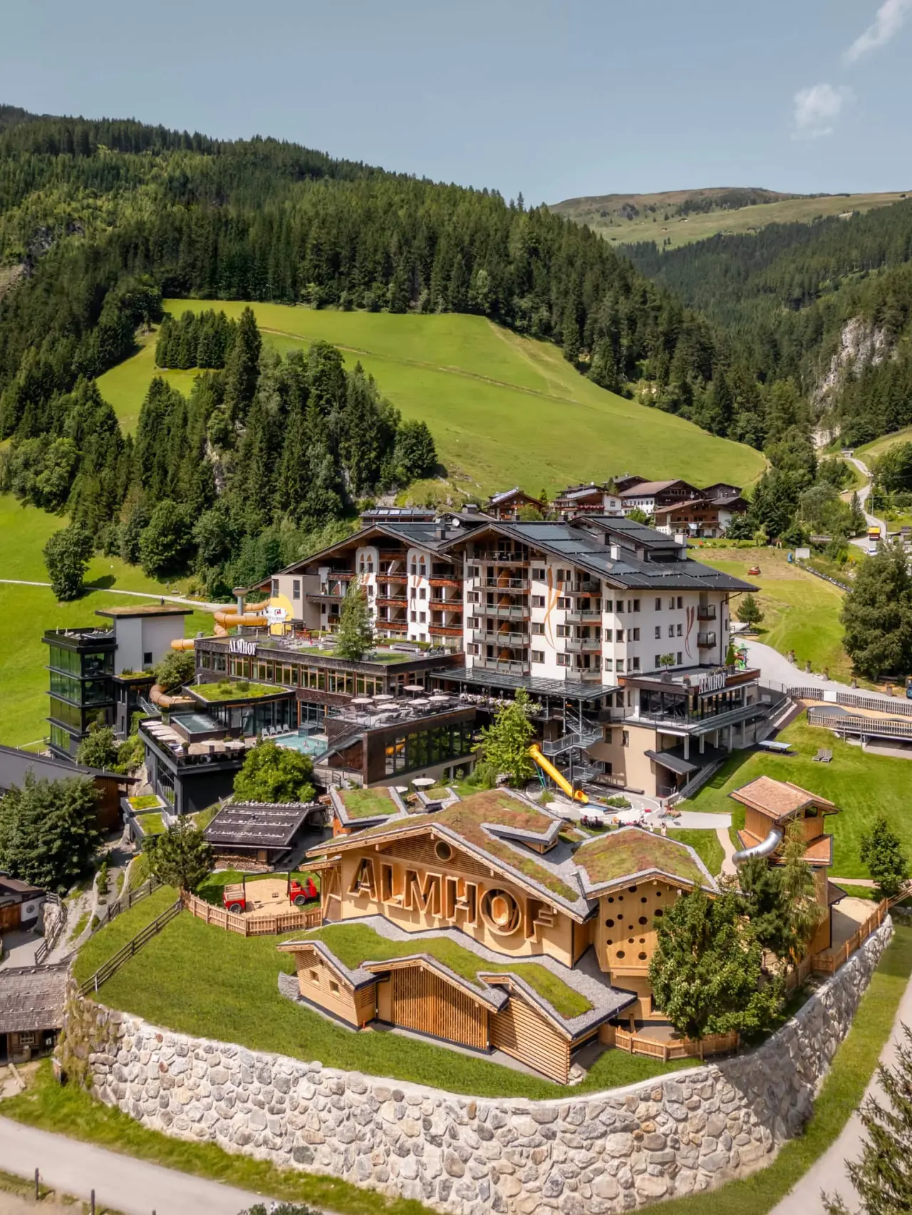 Almhof Family Resort & SPA: Panoramablick auf das luxuriöse Familienhotel mit grünen Dächern, umgeben von Alpenlandschaft.