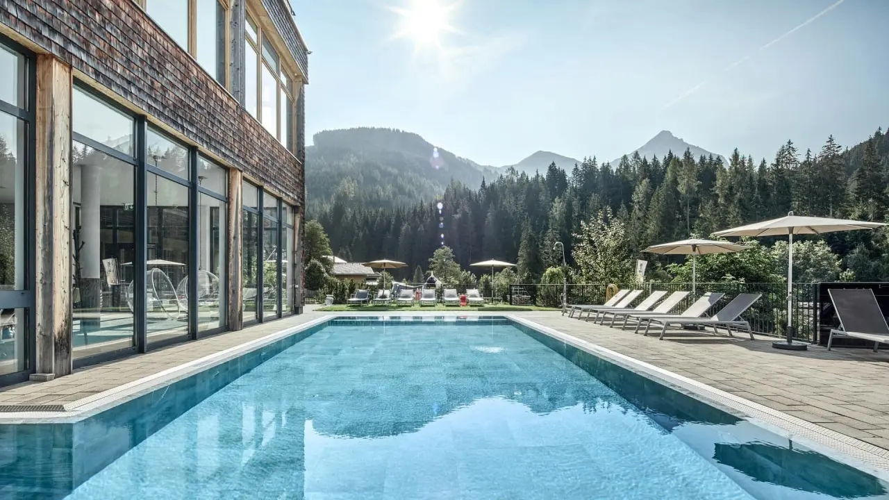 Sonniger Aussenpool mit Liegen und beeindruckendem Bergpanorama im Almhof Family Resort & SPA.