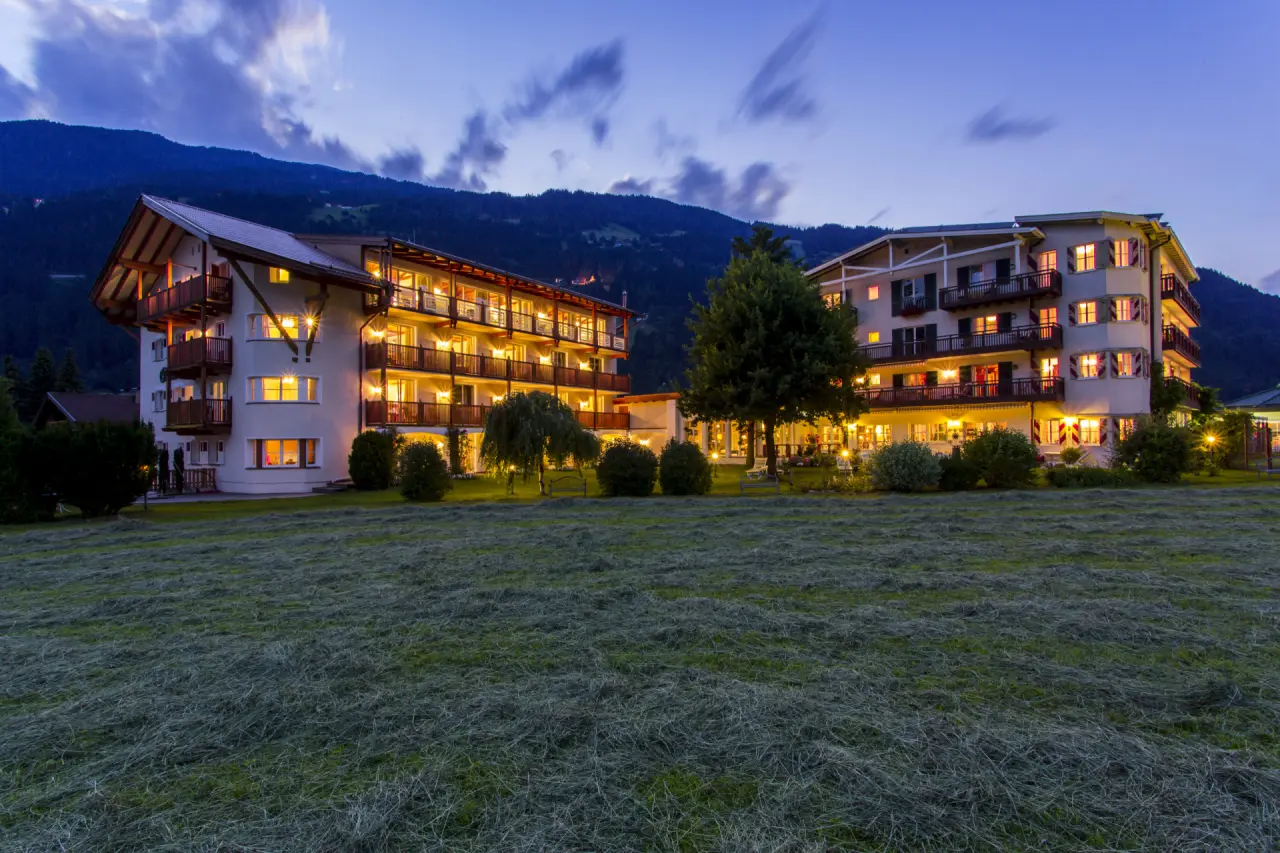 Abendansicht des Genießer-Hotel Theresa mit beleuchteten Balkonen und Bergkulisse bei Dämmerung.