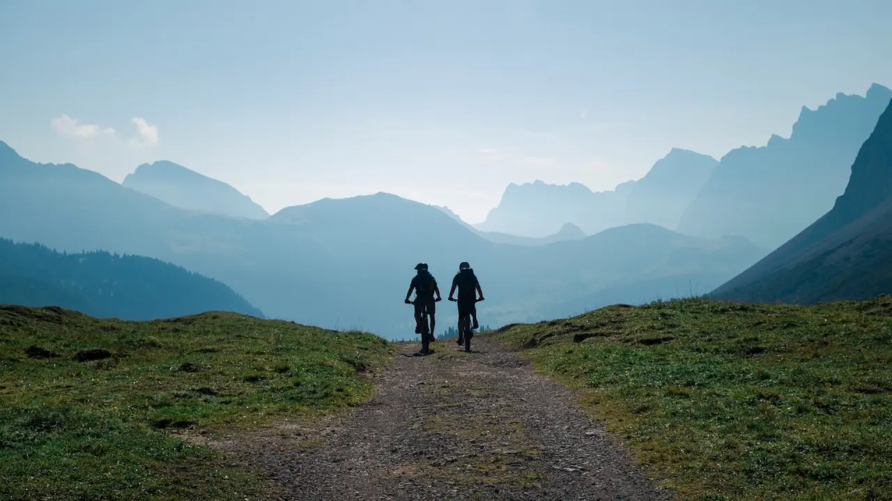 Zwei Mountainbiker auf einem Bergpfad mit weitem Blick auf die Alpenlandschaft rund um Schloss Elmau.