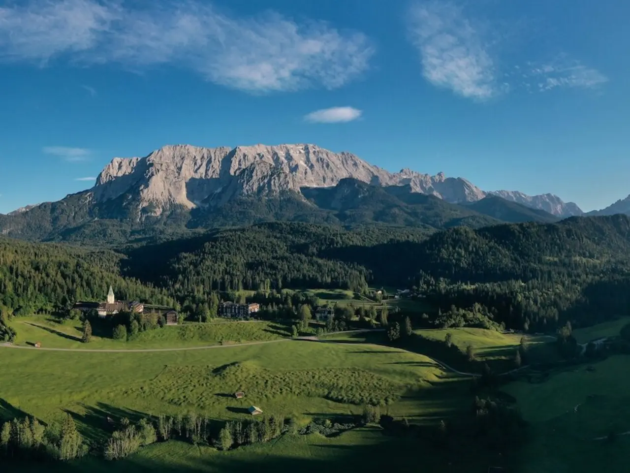Majestätisches Schloss Elmau Resort in den bayerischen Alpen, umgeben von grünen Wiesen und Wäldern unter blauem Himmel.