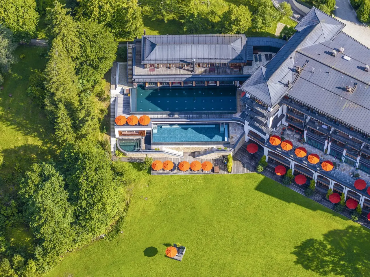 Luftaufnahme des Schloss Elmau mit mehreren Aussenpools, weitläufigen Liegewiesen und grüner Naturumgebung.