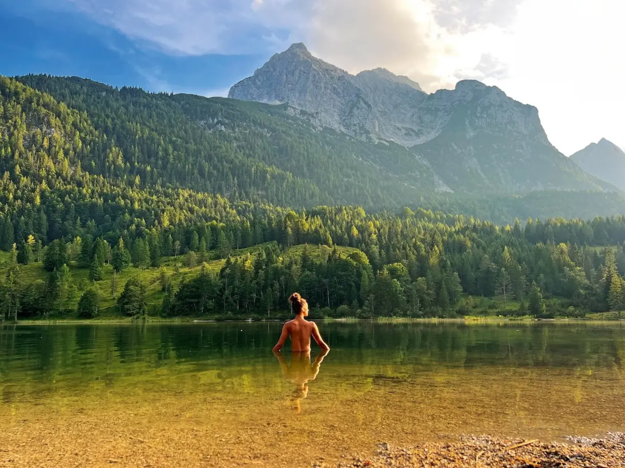 Frau entspannt im klaren Bergsee mit majestätischem Alpenpanorama im Hintergrund, Schloss Elmau.